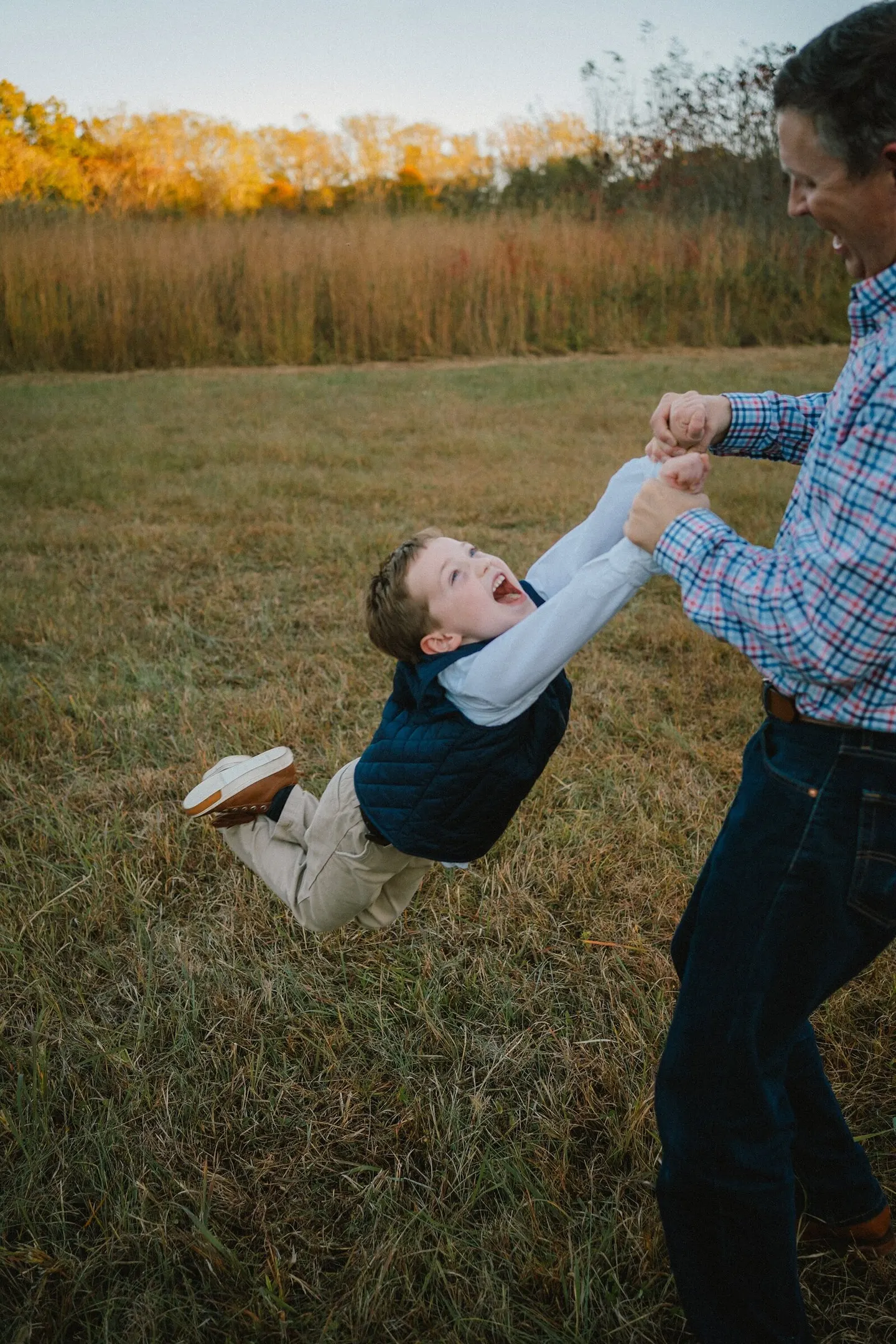 A Charlottesville family photographer captures a father swinging his laughing son through a golden fall field.