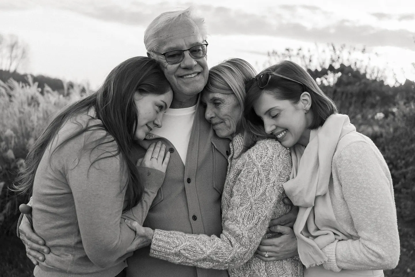Grandparents and their two grown daughters lean in close for a tender embrace on a windy overlook.