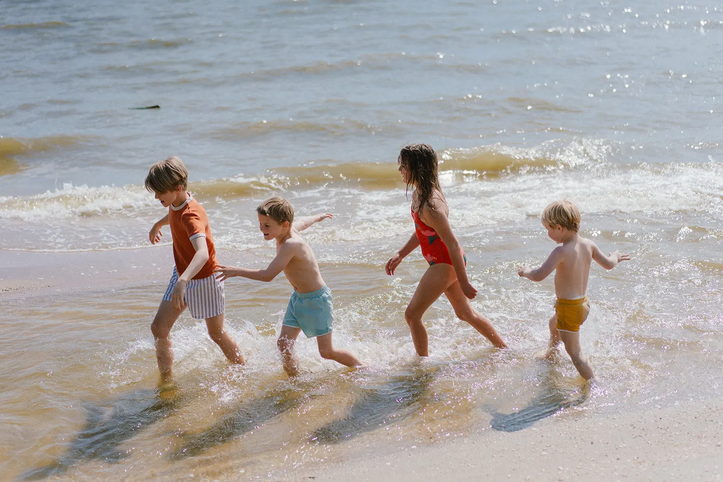 Four kids race through the ocean shallows, waves breaking around their ankles.