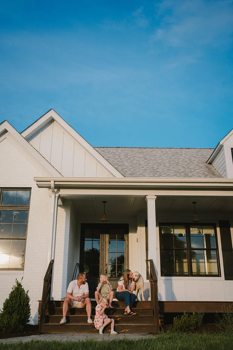 A family of five gathers on farmhouse porch steps with their golden retriever at golden hour.