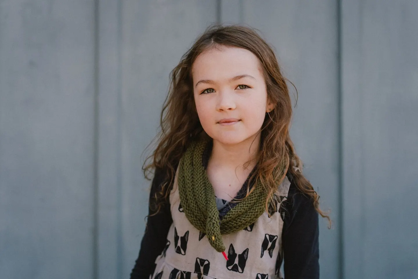 Girl in a hand-knit green scarf against a weathered gray wall