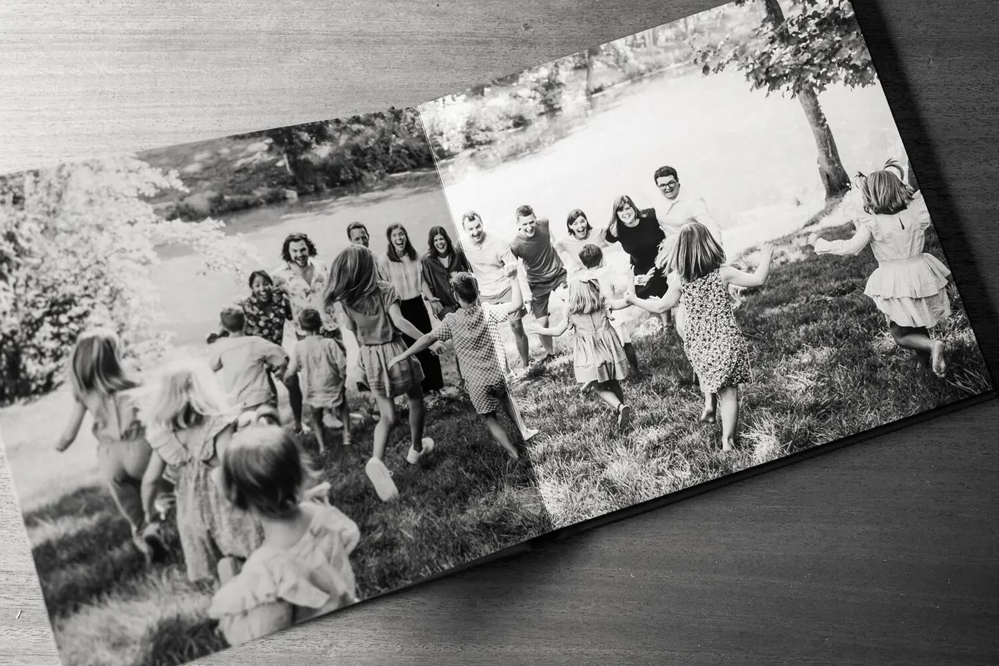 Black-and-white panoramic album spread of an extended family running hand in hand by a river