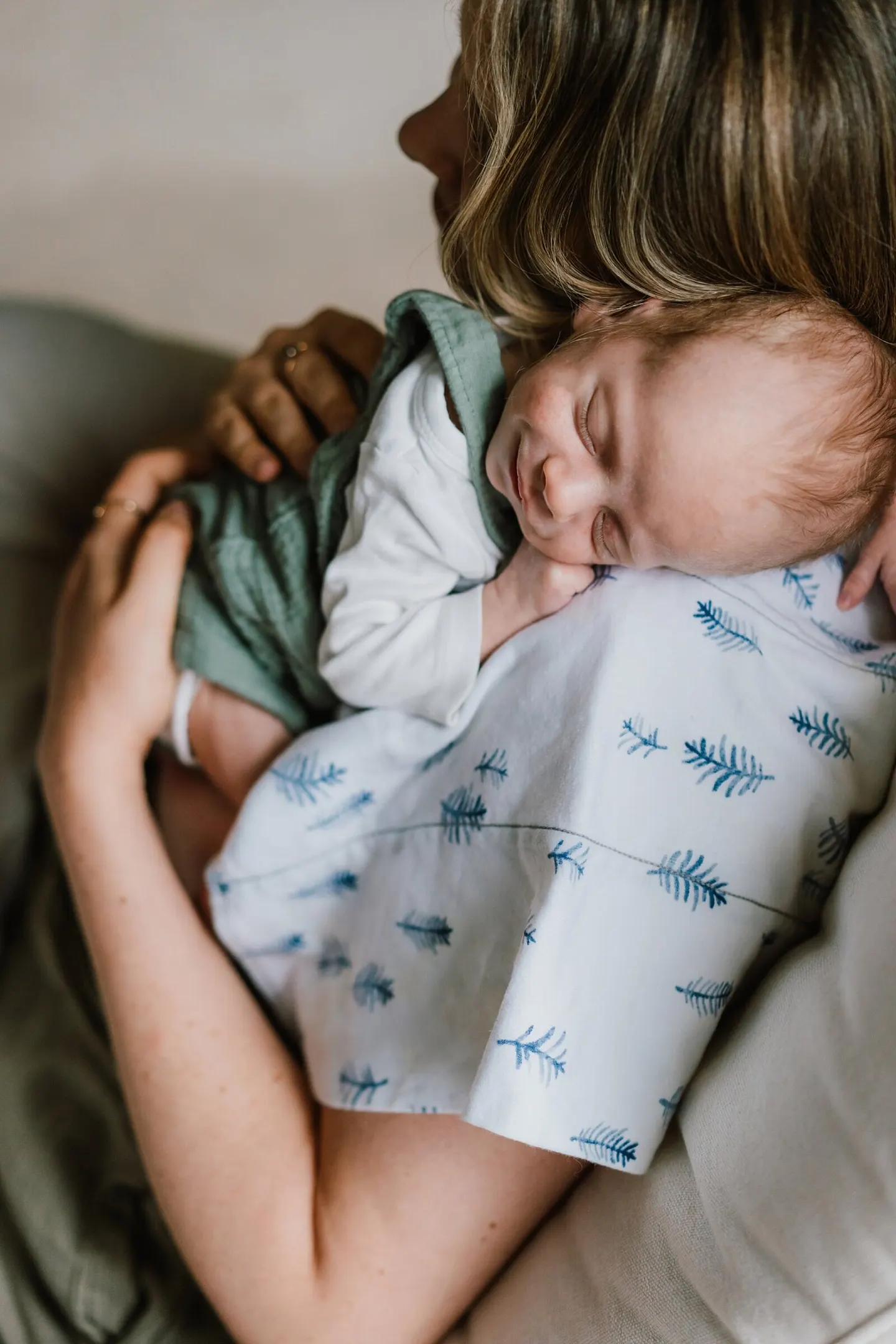 Sleeping newborn nestled on mom's shoulder in a pine-print swaddle