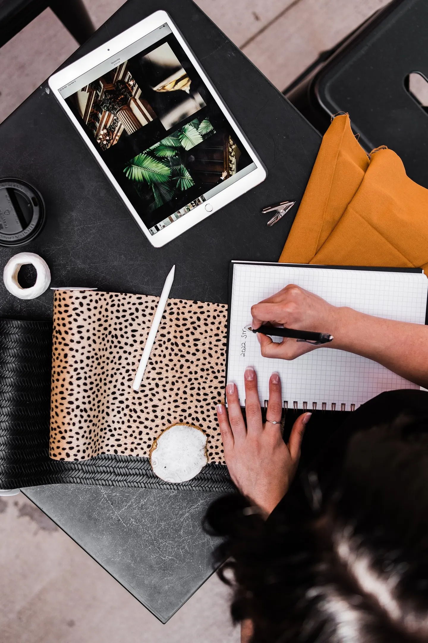 Interior designer sketches notes beside a tablet showing mood-board photos and folded mustard fabric