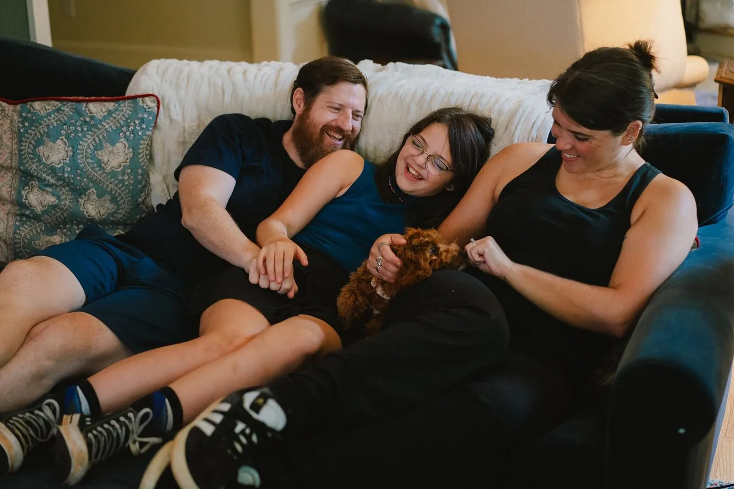 A family of three piles onto the couch, laughing as they cradle their new puppy.