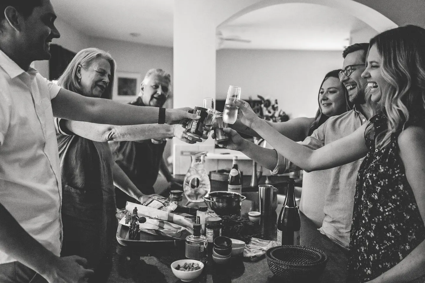 Adult siblings and parents raise glasses together for a toast in a bright, open living room.