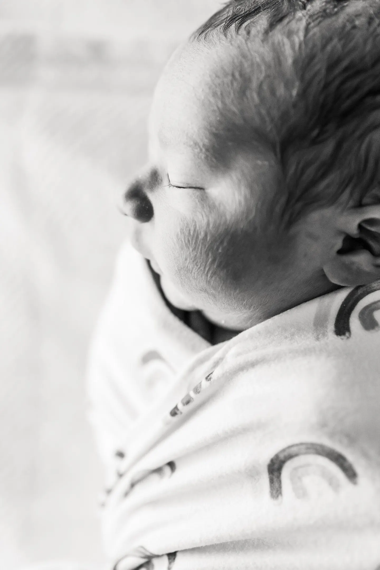 Black and white profile of a sleeping newborn's face against a rainbow-print swaddle