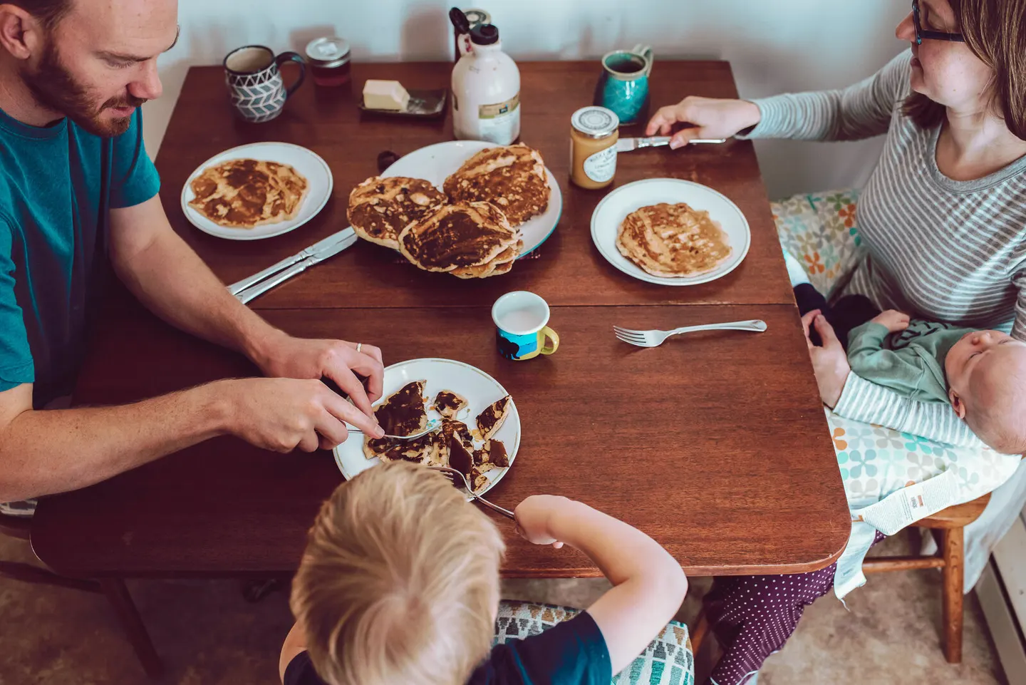 Family sharing pancakes for breakfast at the kitchen table, overhead view