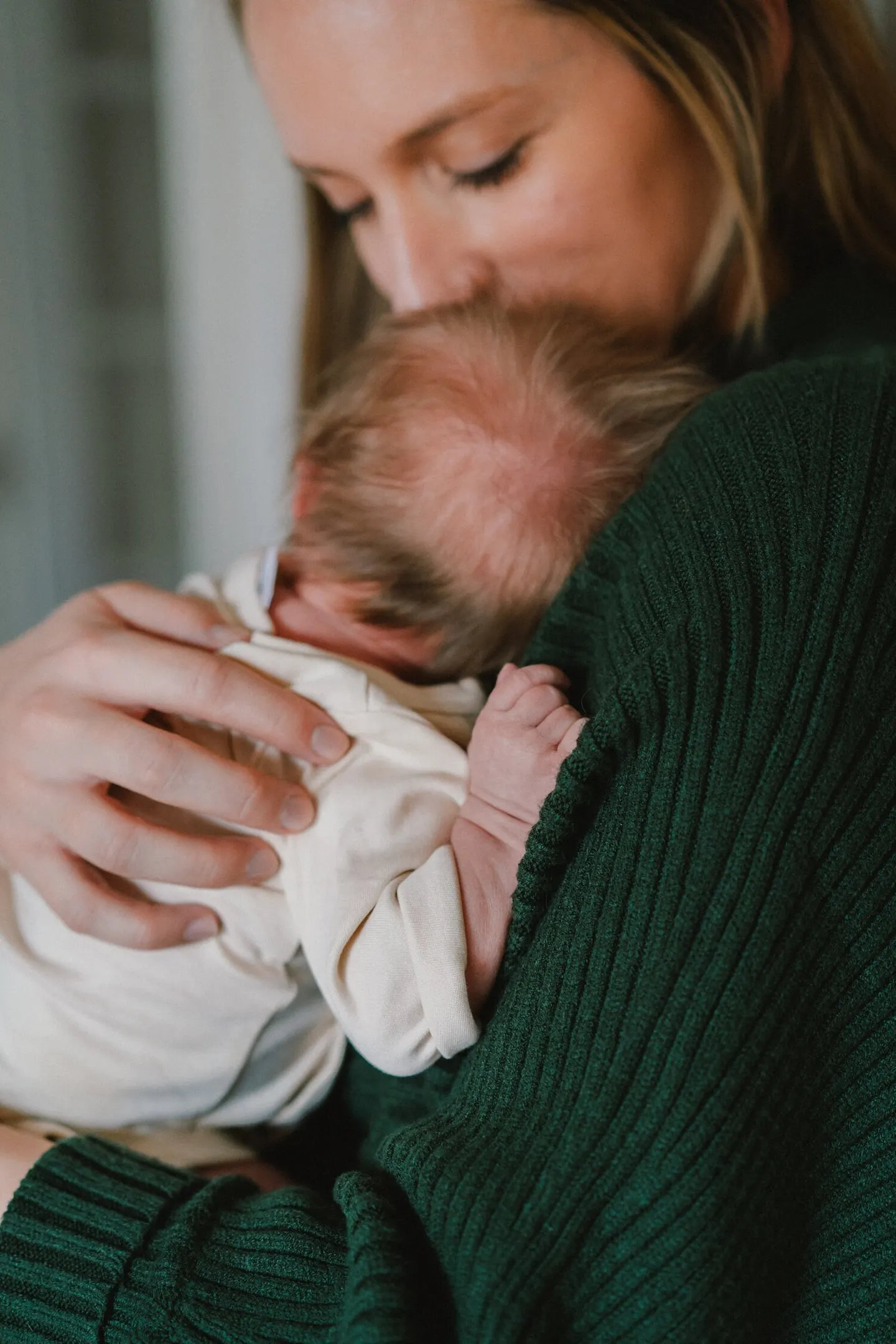 Mother nuzzles her newborn's head, tiny toes peeking from a green sweater