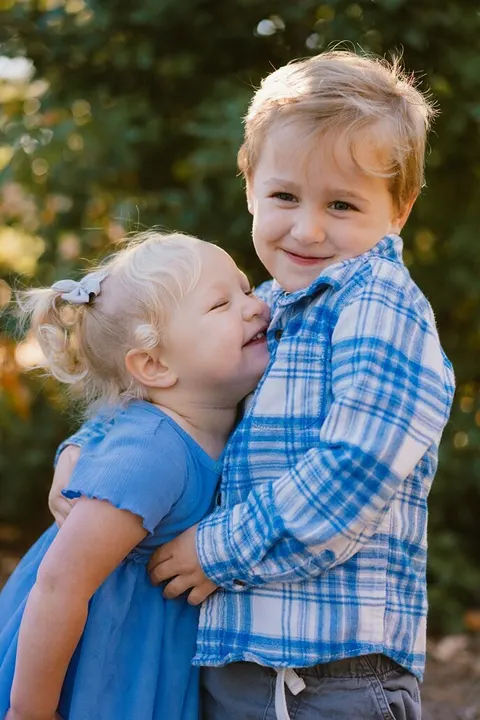 Little sister kissing her brother's cheek, both dressed in blue