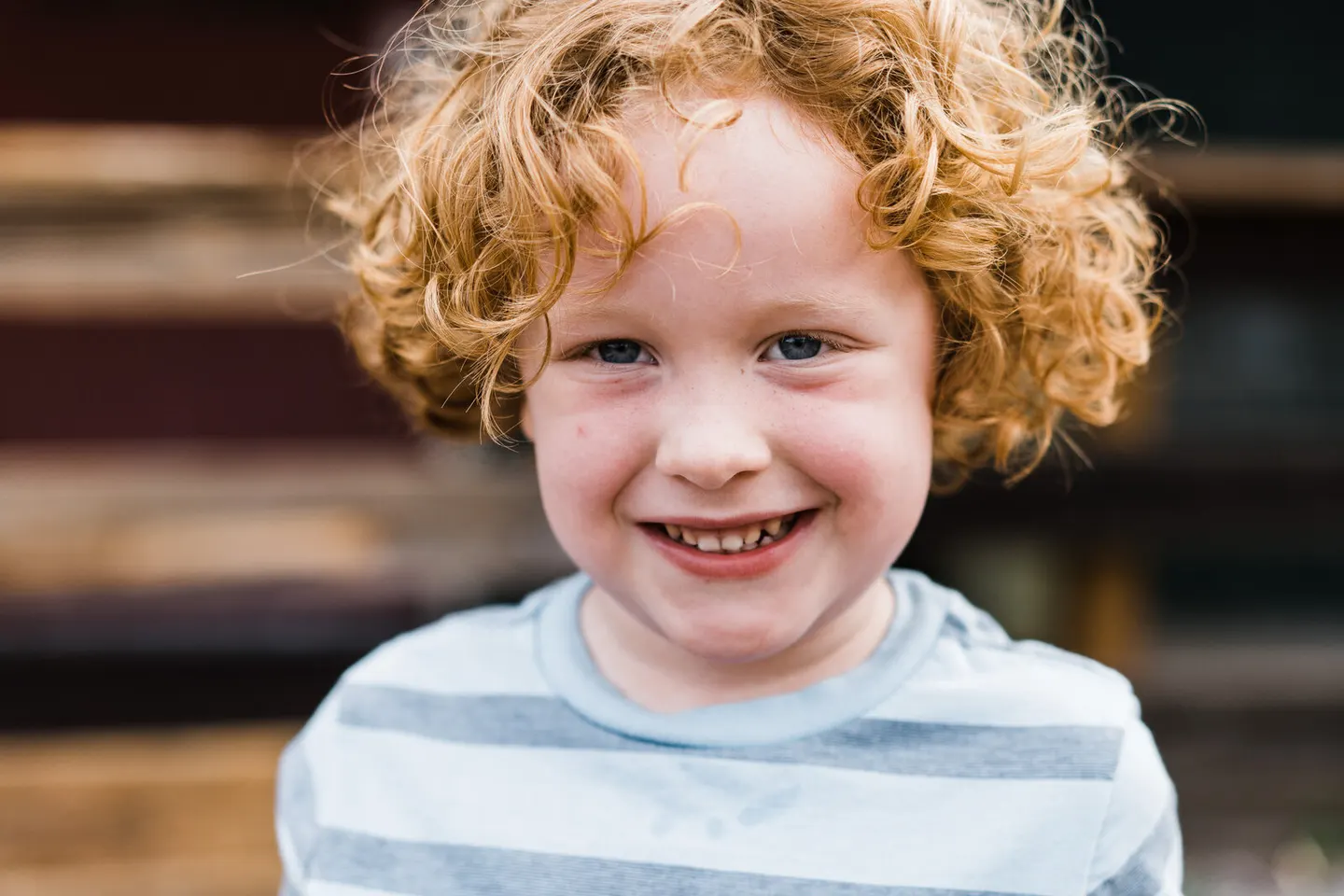 Close-up of a curly copper-haired boy grinning in a striped shirt