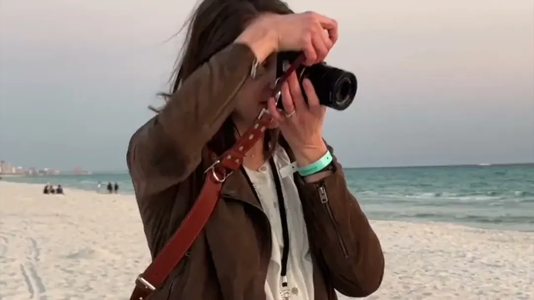 Leah on a beach at sunset, camera raised to her eye, photographing a family