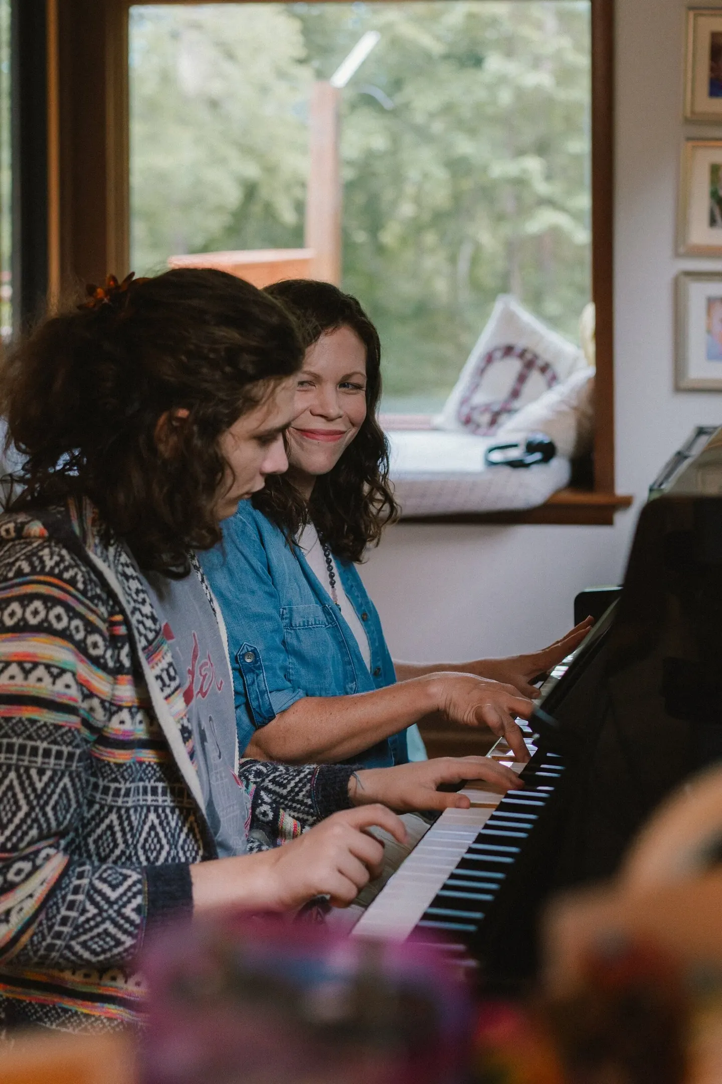 Two women share a laugh while playing piano together.