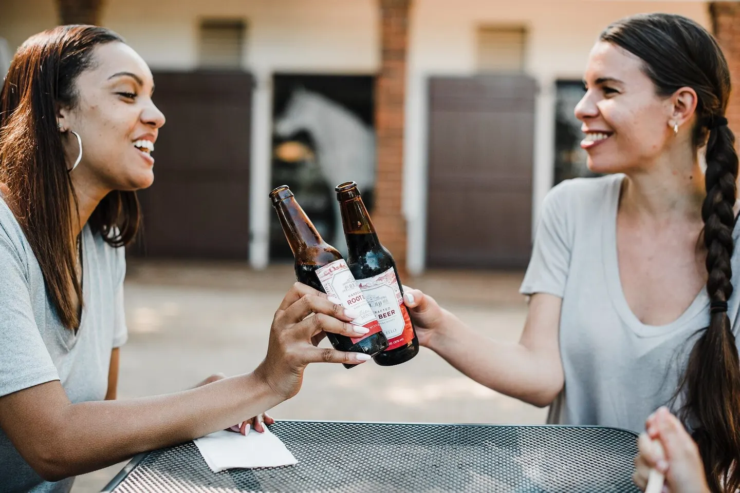 Two business partners clink coffee mugs laughing at a sunny outdoor cafe table