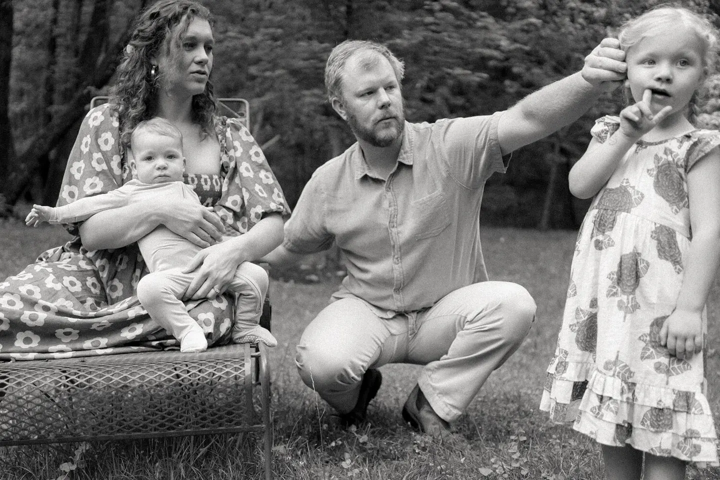 In black and white, a girl holds a finger to her lips beside her parents and baby sibling.