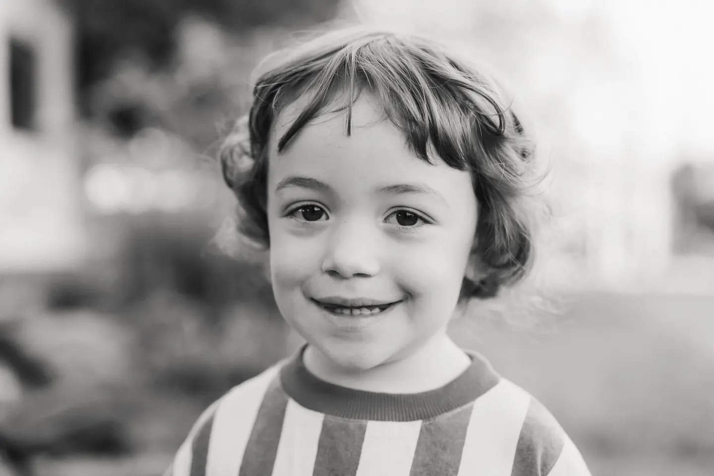 Black-and-white portrait of a curly-haired boy smiling softly outdoors