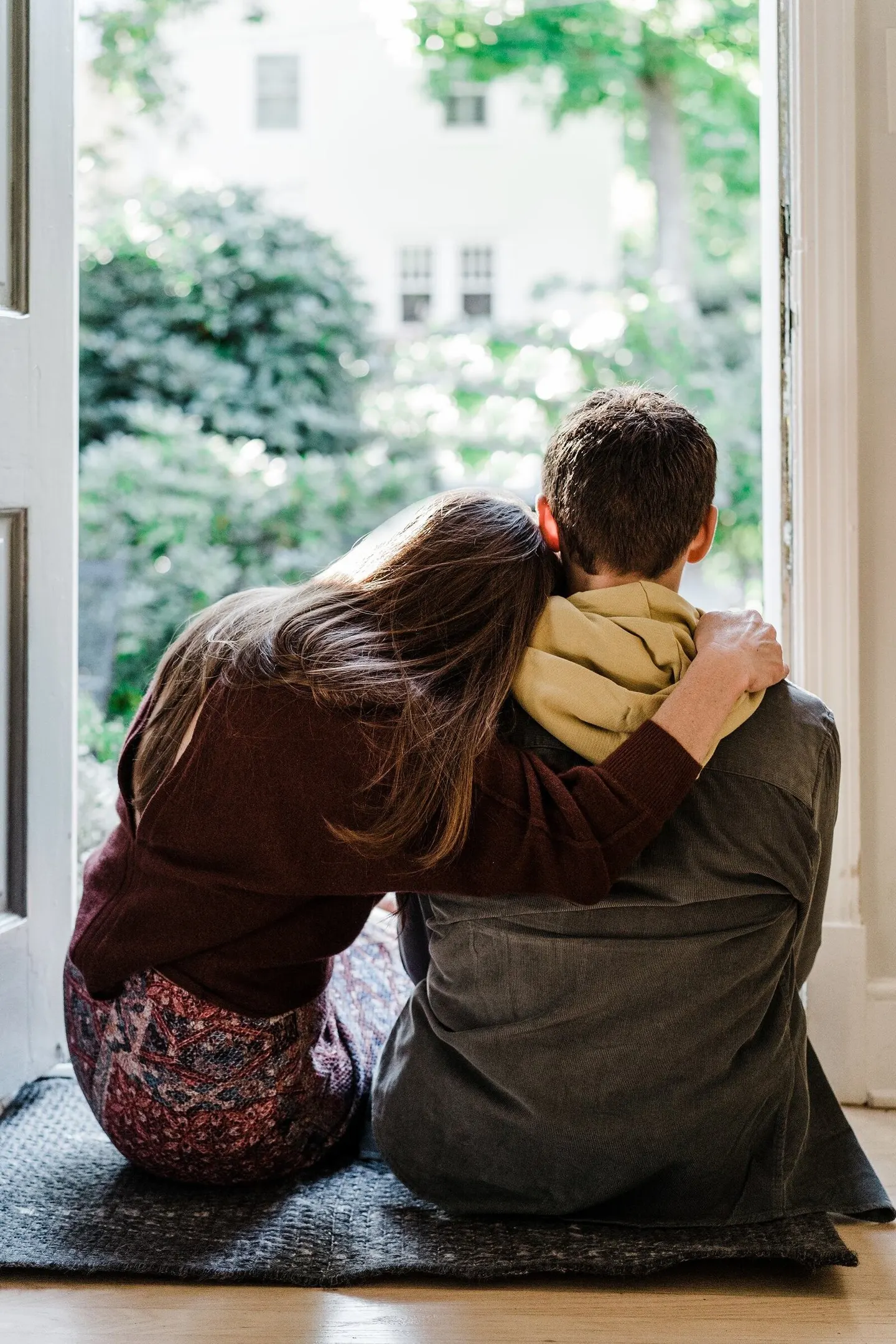 Seen from behind, a couple embraces in an open doorway, looking out at the green garden beyond.