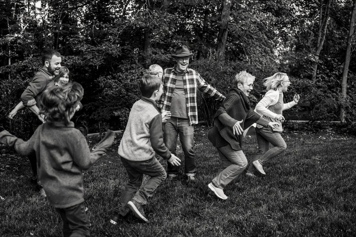 A family breaks into a joyful run across the lawn together, grandparents and grandkids laughing mid-stride.