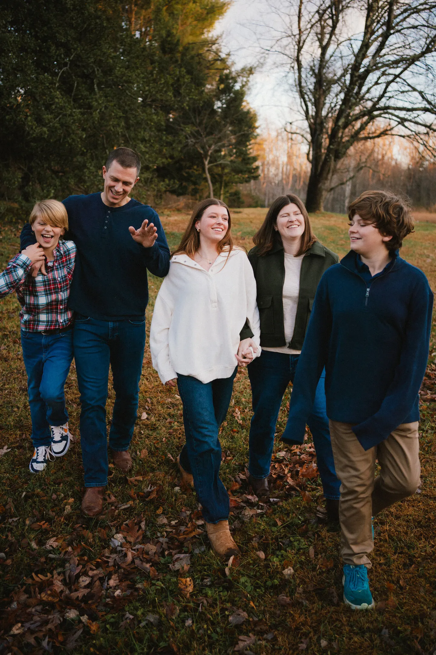 A family of five laughs mid-stride through a leaf-strewn autumn field as golden hour light fades.