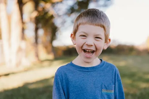 Boy grinning outdoors in a blue t-shirt at Mountaintop School