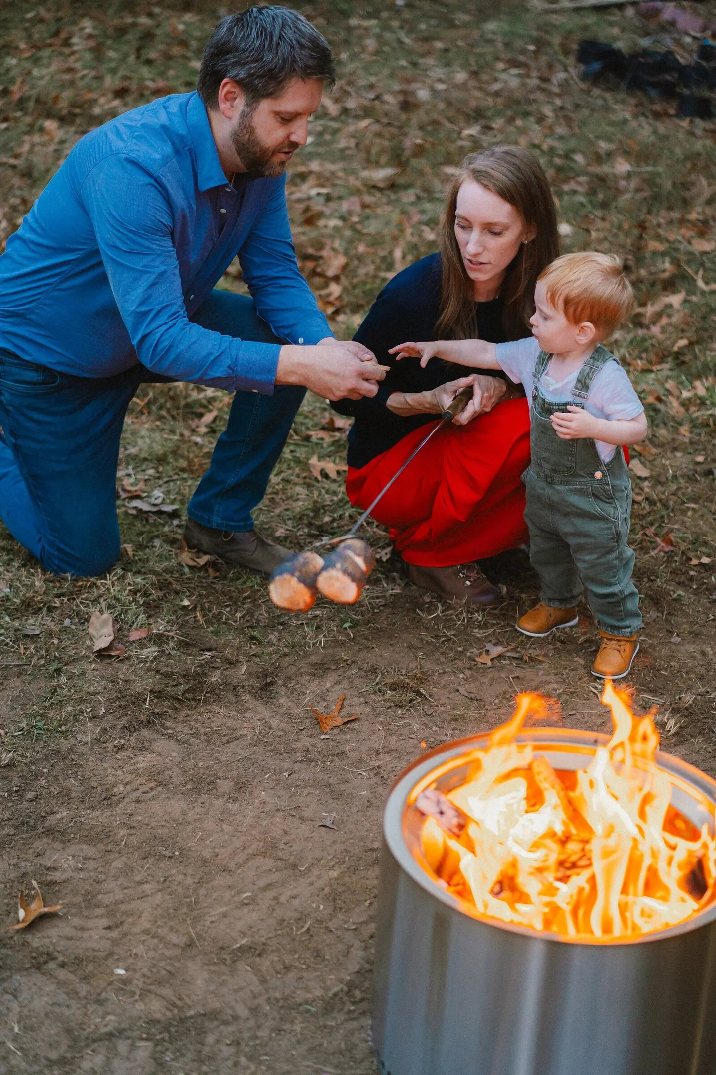 A family gathers around a crackling firepit, roasting marshmallows as their toddler reaches in.