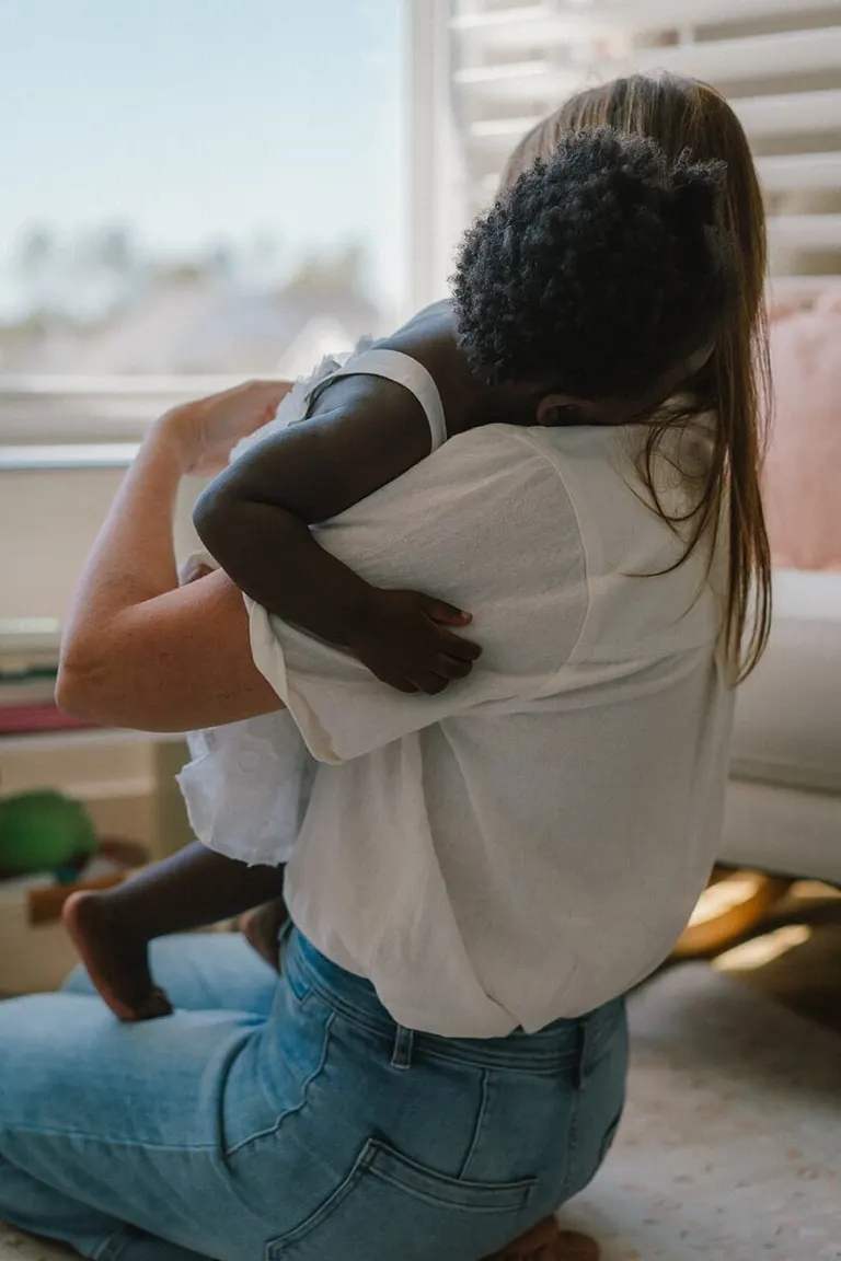 Mom hugging her curly-haired toddler in a sunlit bedroom