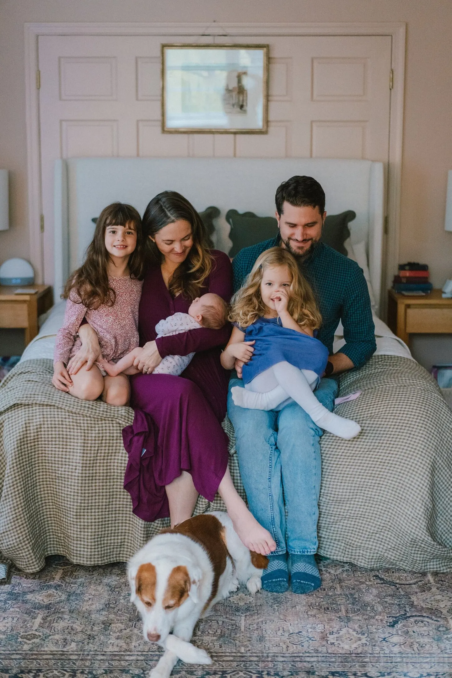 Family of five plus their spotted dog gather on the bed to welcome a newborn