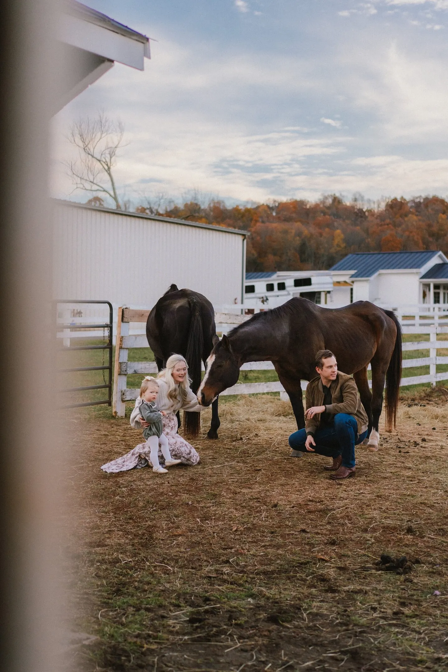 Grandparents and a toddler greet two horses at the fence, autumn color filling the barnyard.