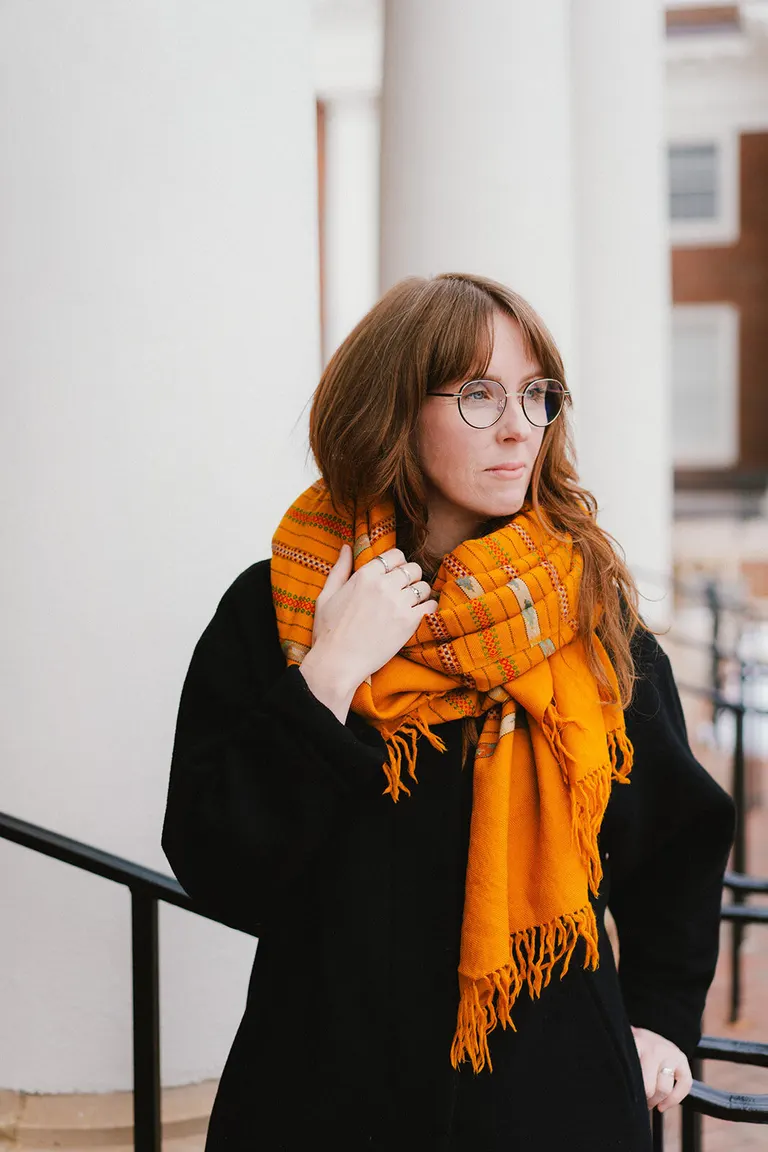 Woman in round glasses and a mustard scarf gazes down a sunlit colonnade, Charlottesville photographer portrait