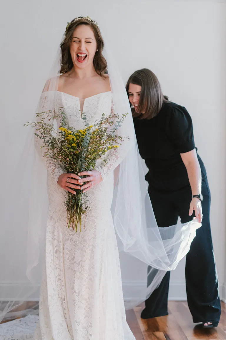 Bride laughing joyfully as her wedding planner arranges her veil before the ceremony