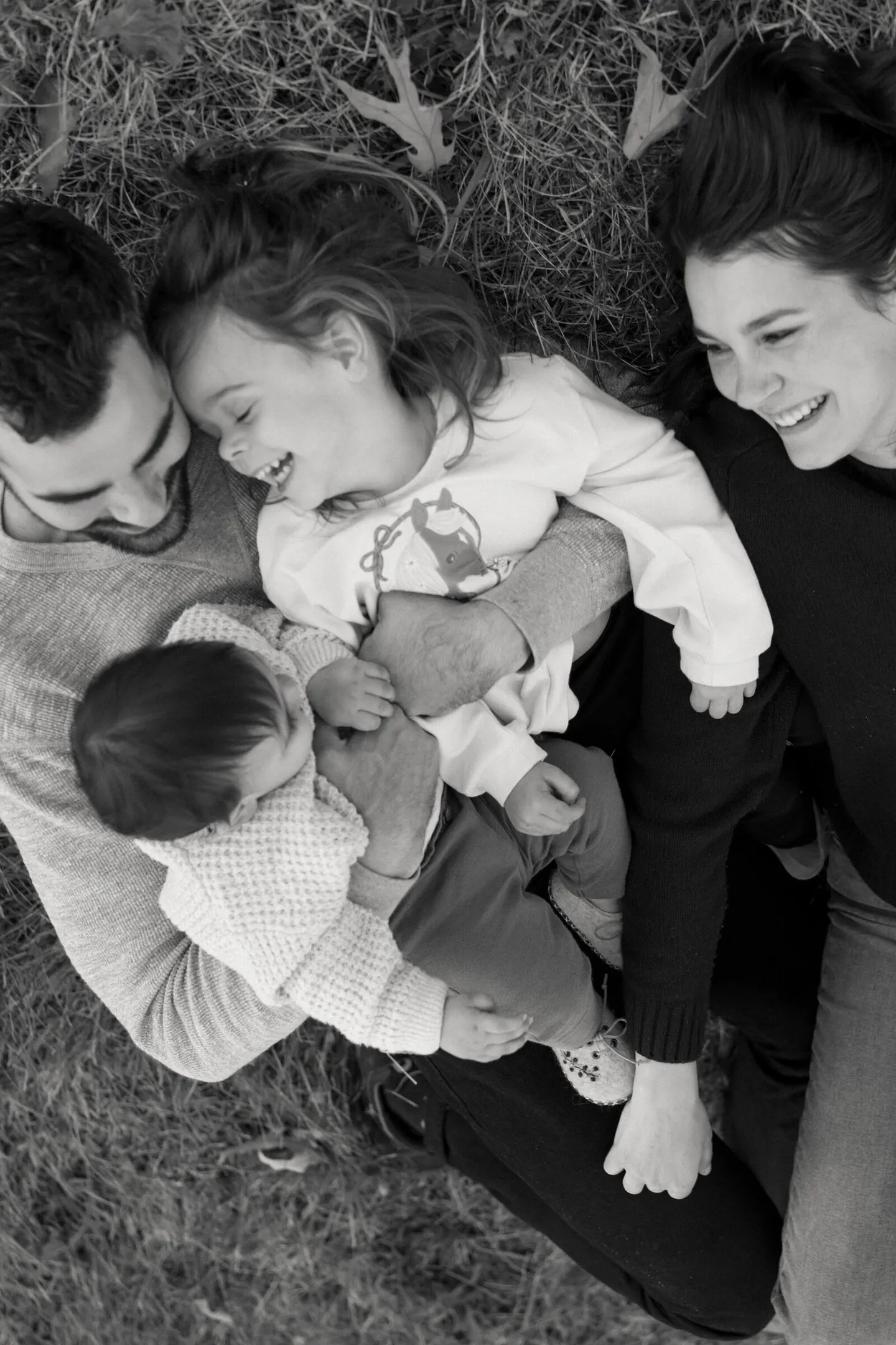 Seen from overhead in black and white, a family of four lies together in the grass.