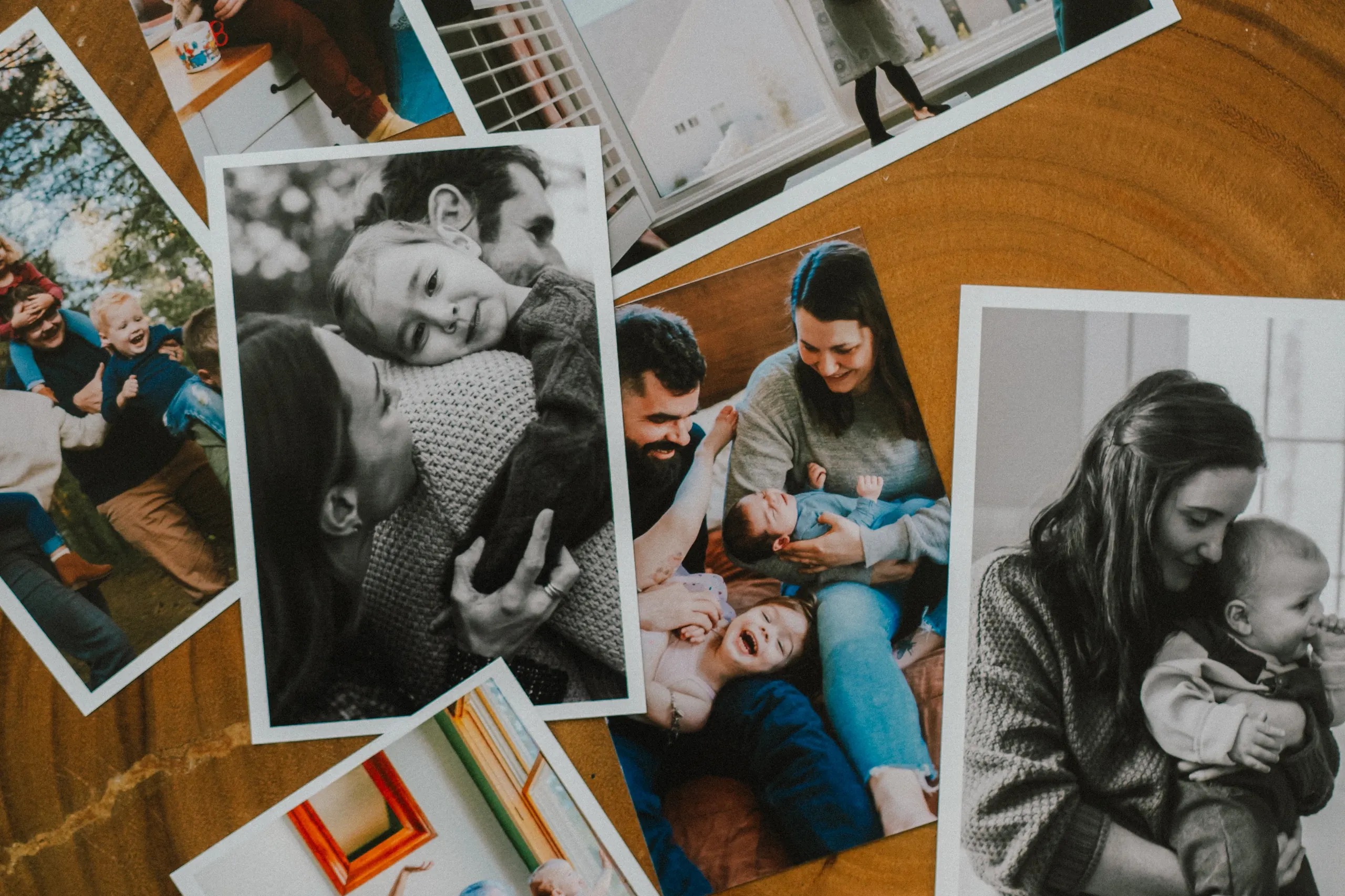 A spread of printed family photographs fanned out across a wood slab, in colour and black and white.