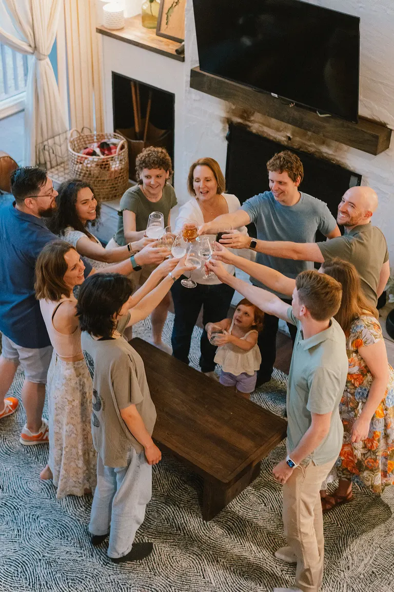 An overhead view catches a large family lifting their glasses together in a toast at a reunion.