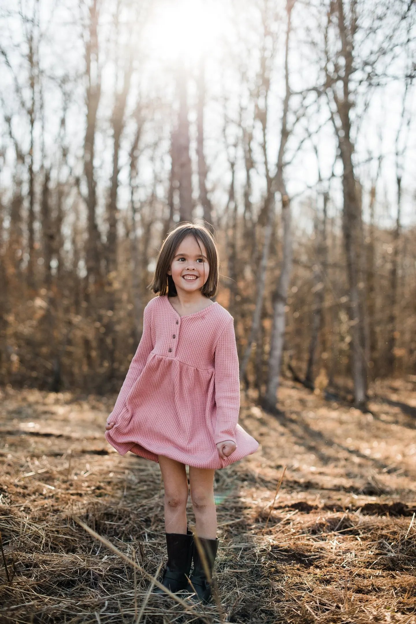 Girl in a pink dress twirling through a sunlit forest clearing
