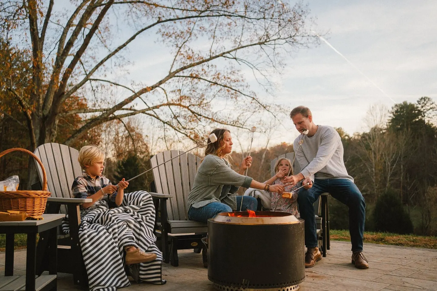 Family roasting marshmallows around a fire pit on a fall evening