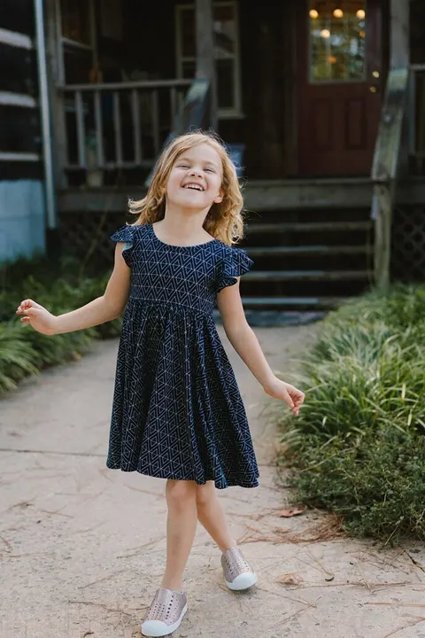 Girl laughing in a navy print dress on a porch pathway