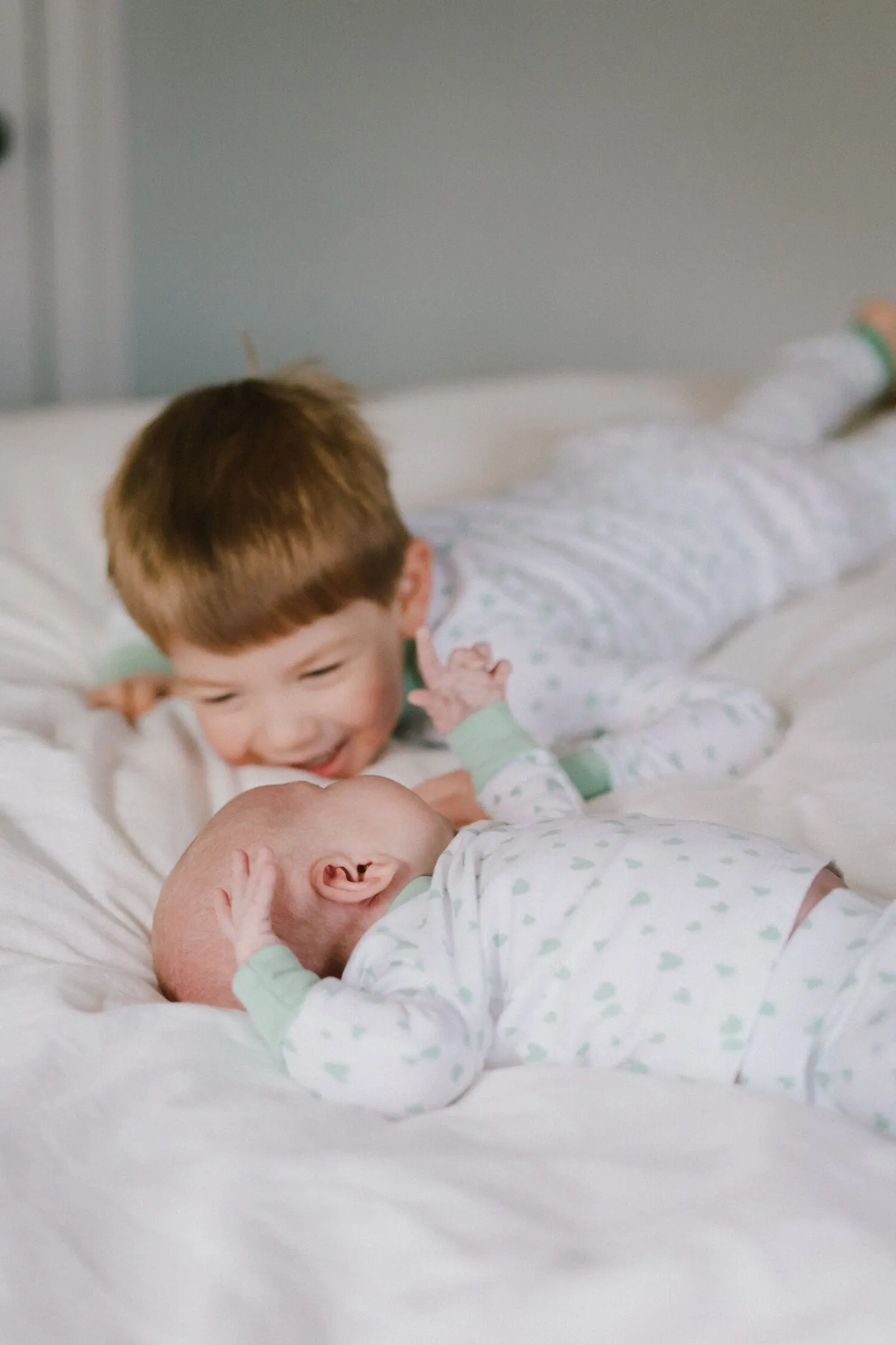 Newborn on a bed reaches up while his grinning big brother looks on