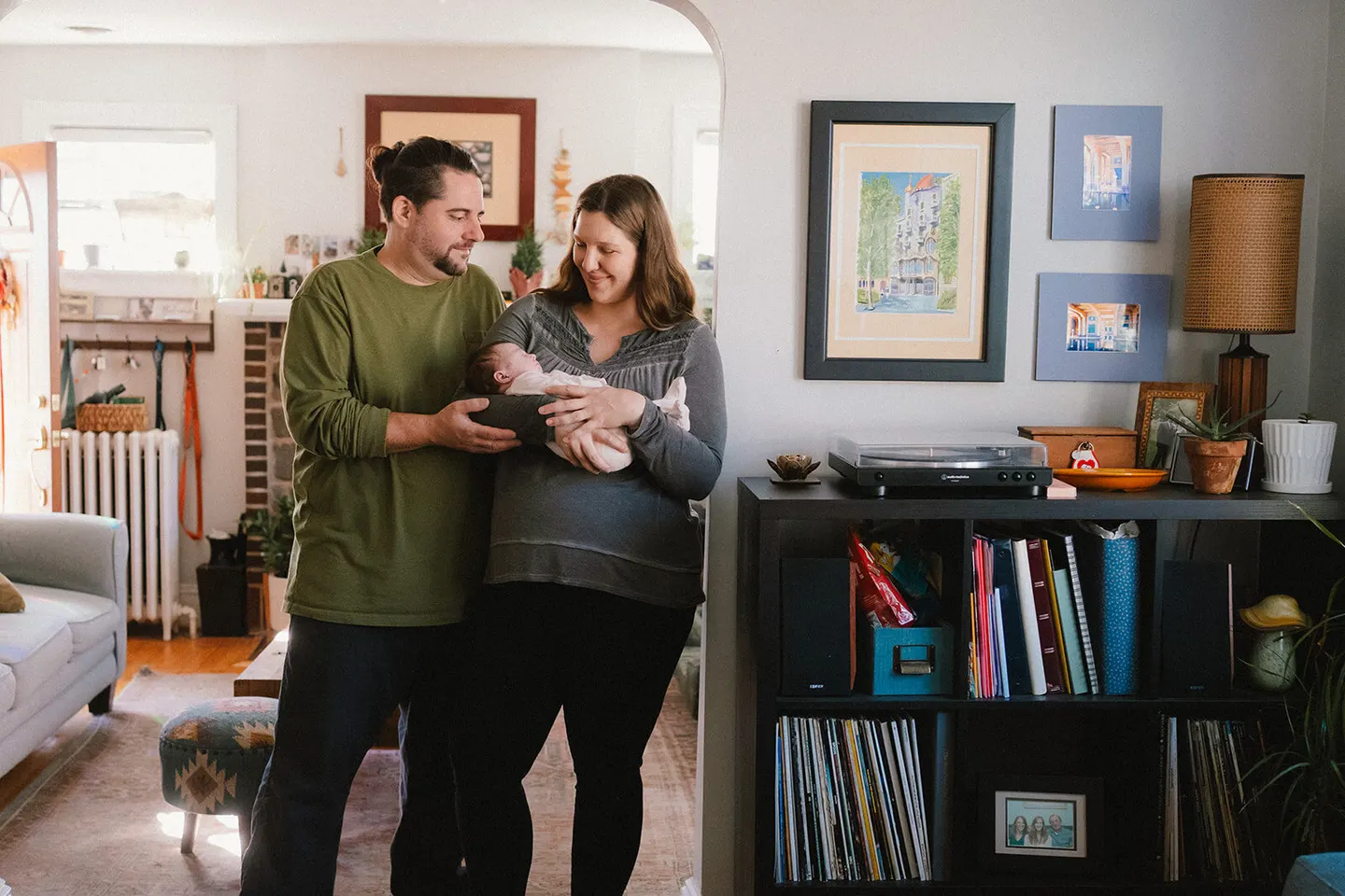 Charlottesville photographer frames new parents admiring their baby in a sunlit living room archway