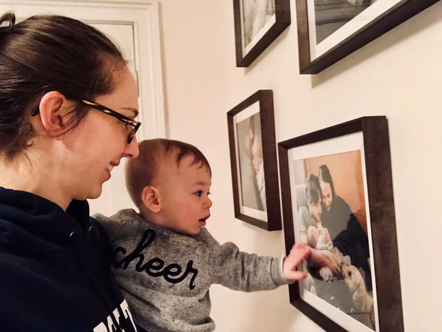Toddler reaching to touch a framed print of his parents cradling a newborn on a gallery wall