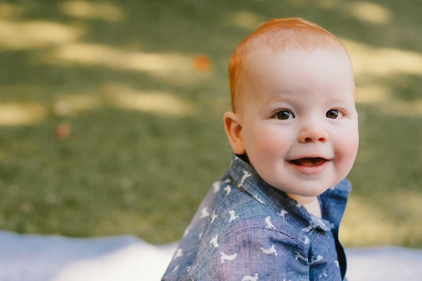 Redheaded baby grinning in a blue rabbit-print shirt
