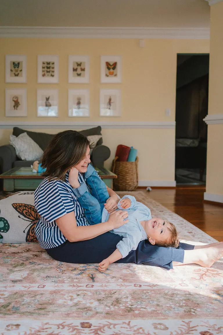 A Charlottesville family photographer catches a mother and baby laughing together on a living room rug.