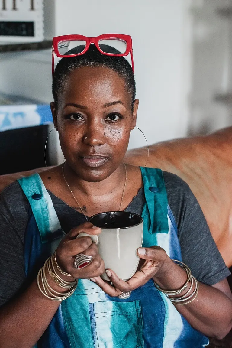 Portrait of a woman with red glasses pushed back into her hair, holding a mug of coffee
