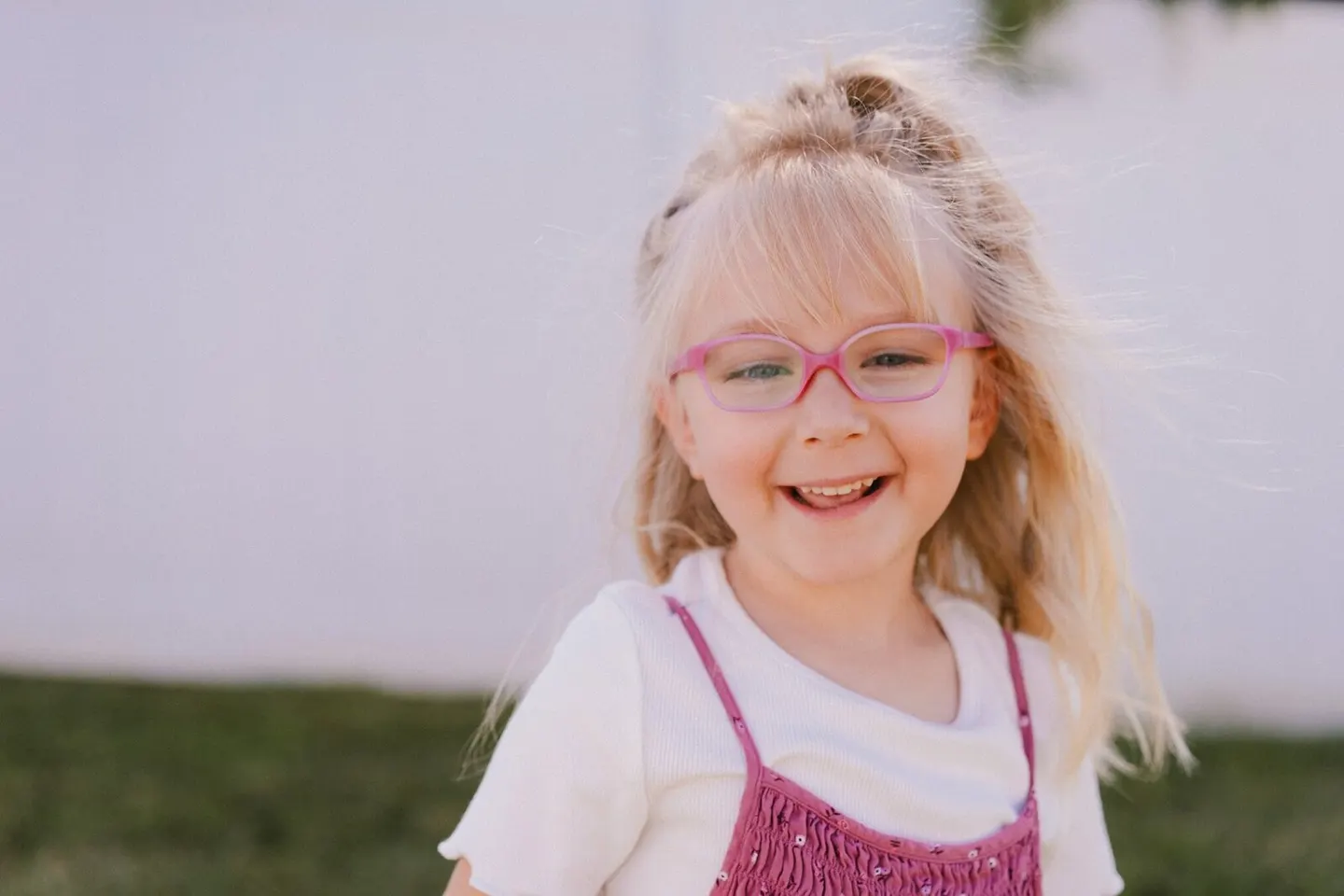 Girl in pink glasses smiling with windblown hair at Bright Beginnings