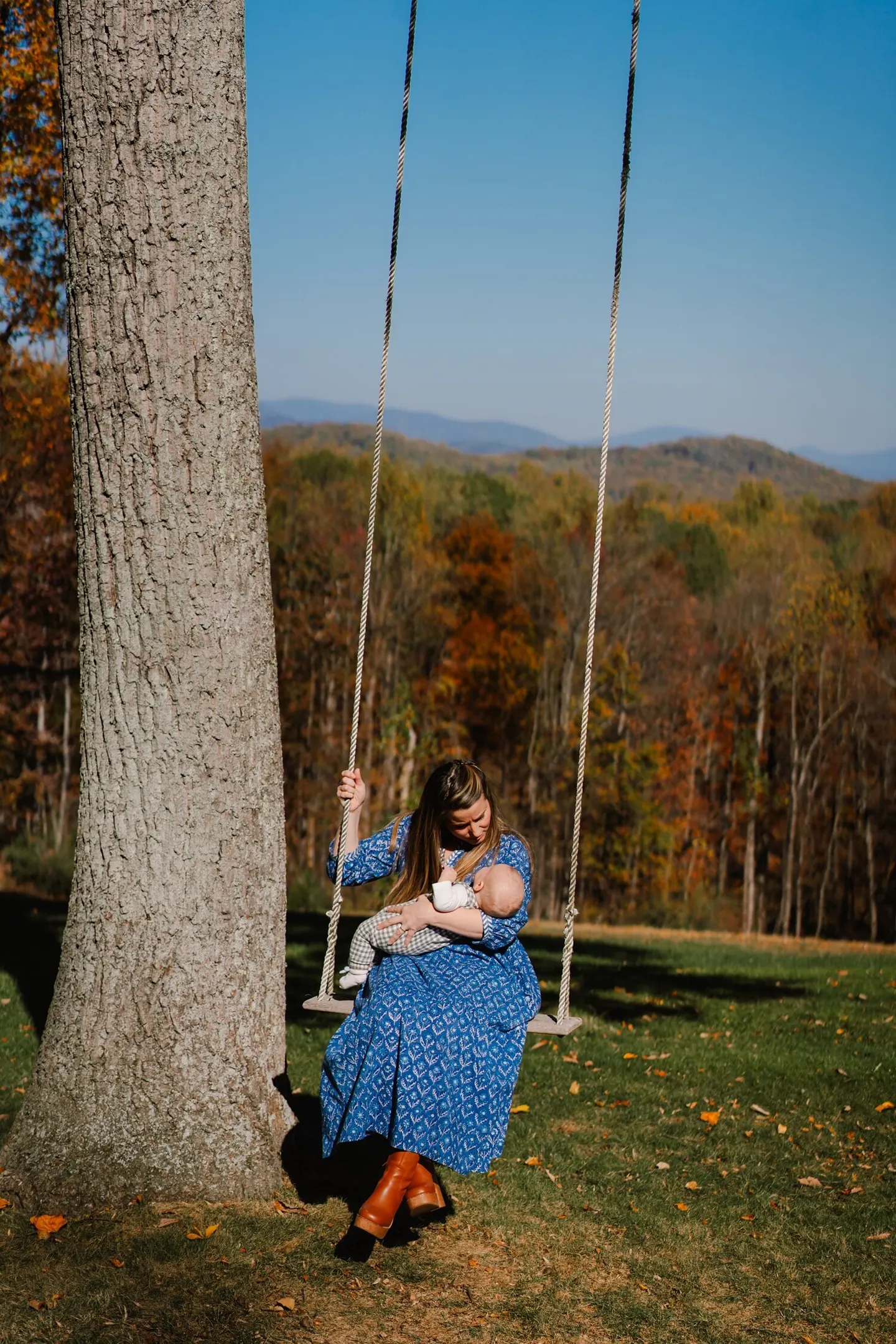 Mother nurses her baby on a tree swing overlooking layered Blue Ridge foothills