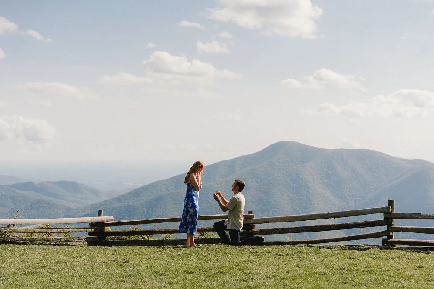 A man kneels to propose on a mountain overlook, the Blue Ridge stretching out behind them.