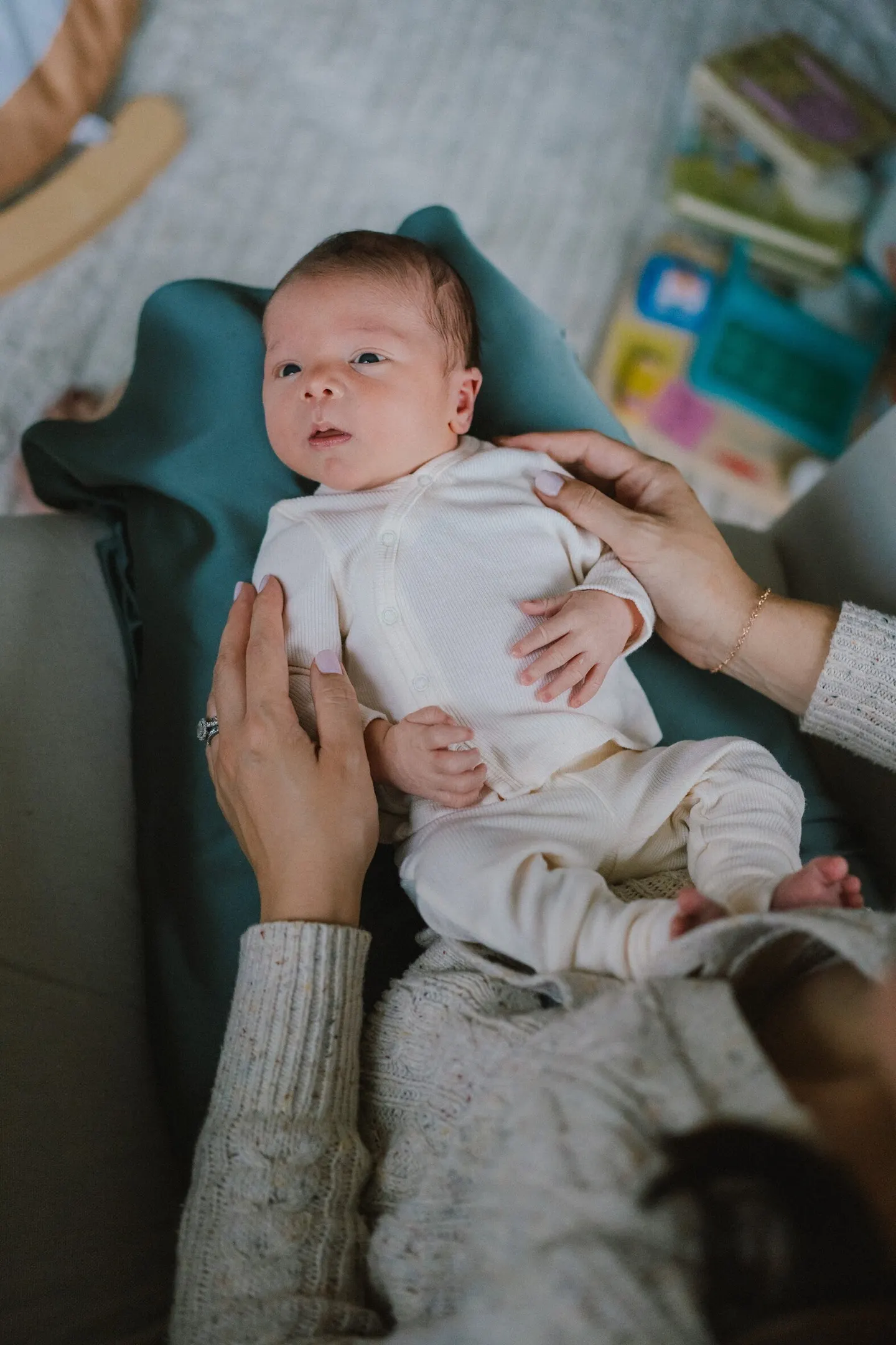 Newborn photographer poses a wide-eyed infant on a teal cushion beside wooden toys