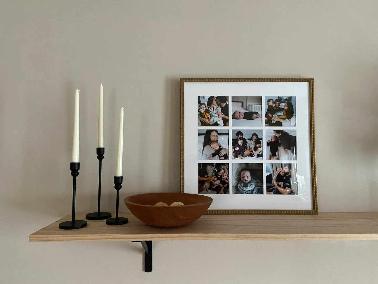 Nine-panel gold grid frame of newborn moments displayed on a floating wood shelf with candles