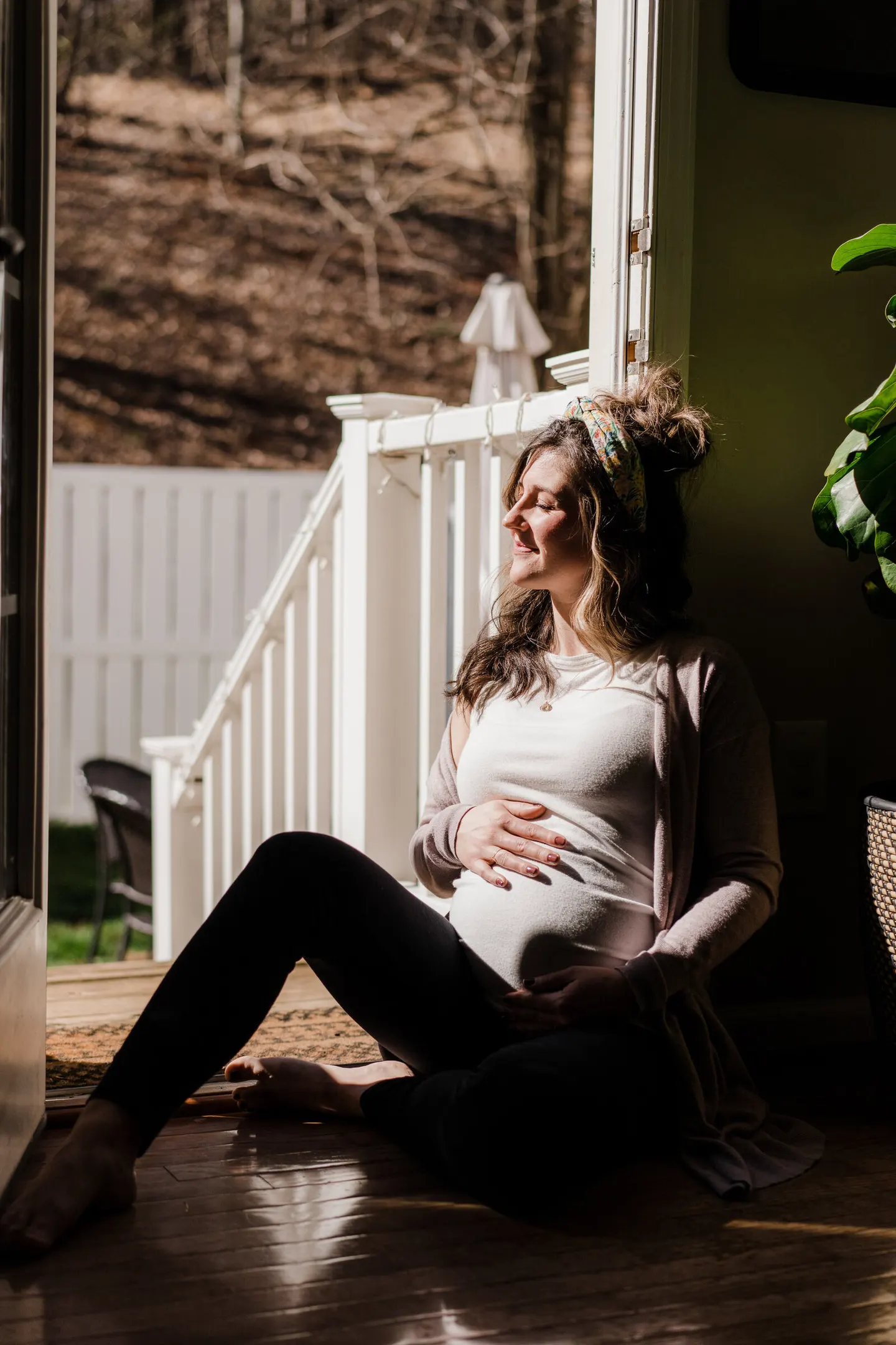 Pregnant woman rests against a doorway in golden afternoon light, hand on her belly
