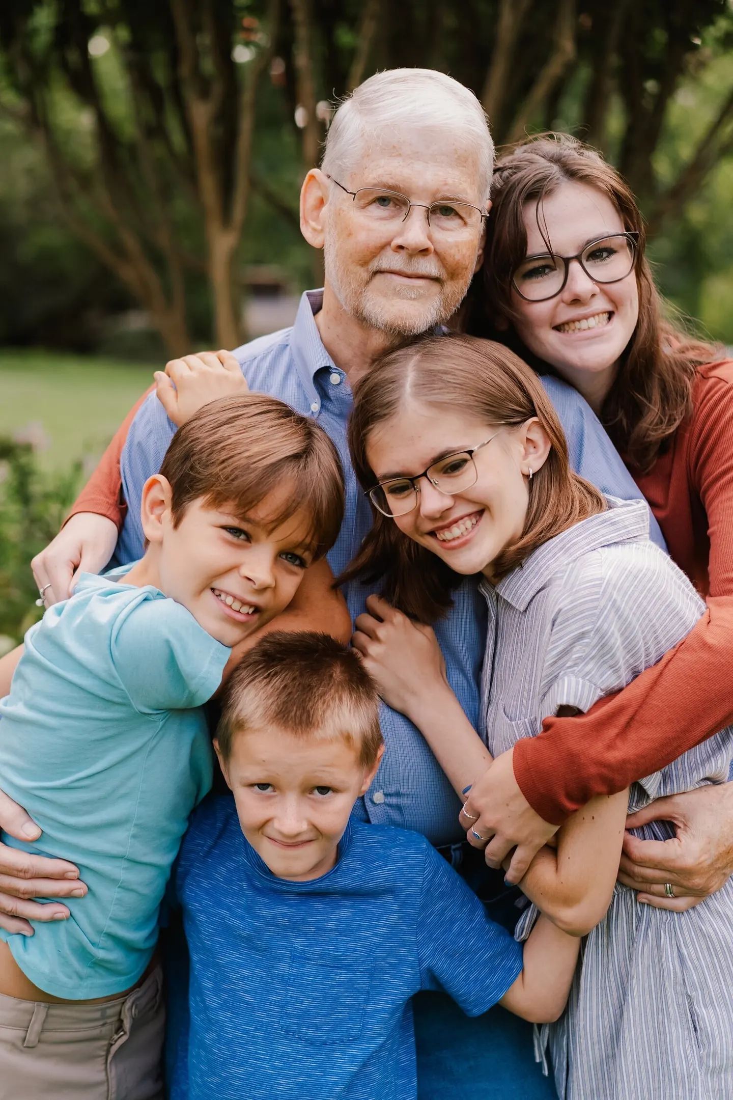 Three generations pile into a close group hug outdoors, cheeks pressed together and smiling.