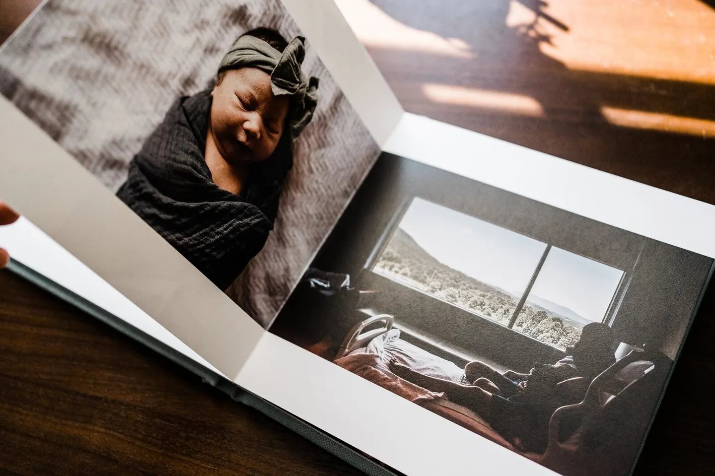 Open album on a wood table, a swaddled newborn on one page and a mountain-view nursery on the next
